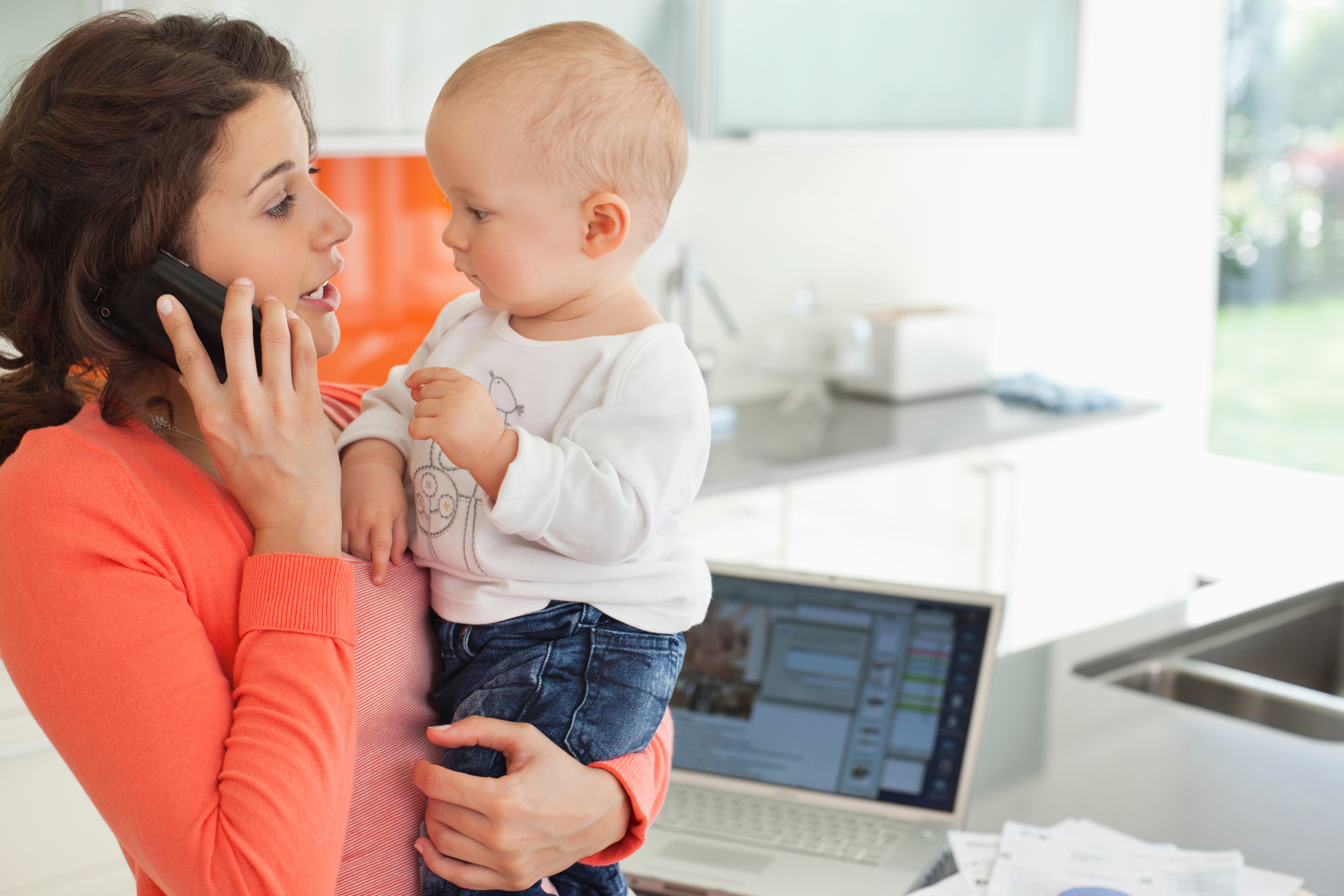 female-european-adult-indoor-holding-baby-while-talking-on-mobile-phone-web